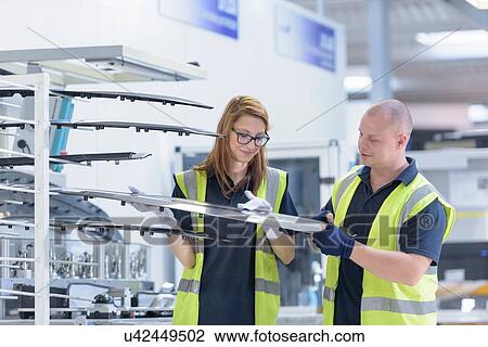 Stock Image - Workers checking paint finish on automotive parts in spray paint factory. Fotosearch