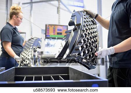 Stock Image - Workers checking paint finish on automotive parts in spray paint factory. Fotosearch