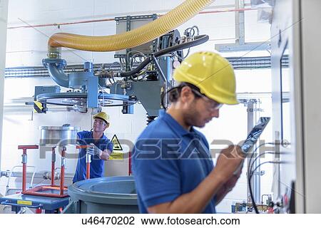 Stock Image - Workers operating environmental testing equipment with digital tablet in electronics factory. Fotosearch