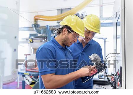 Stock Image - Workers operating environmental testing equipment with digital tablet in electronics factory. Fotosearch