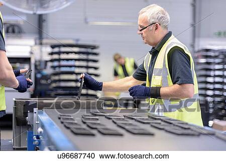 Stock Image - Workers with automotive parts in spray paint factory. Fotosearch