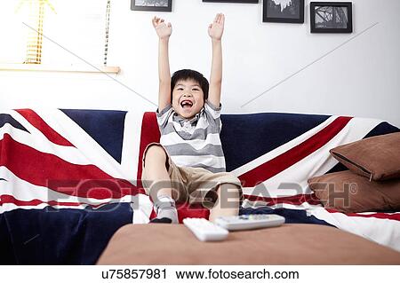 Young boy sitting on sofa watching and cheering at television at home View Large Photo Image Stock Image - Young boy sitting on sofa watching and cheering at television at home. Fotosearch