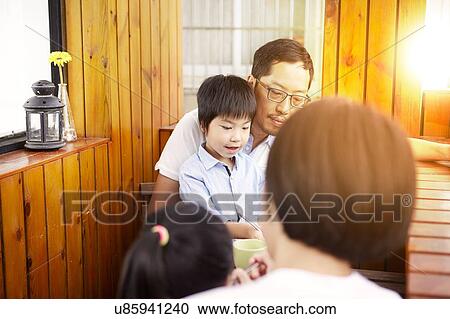 Stock Image - Young Chinese family having breakfast on the balcony in the sunshine together. Fotosearch