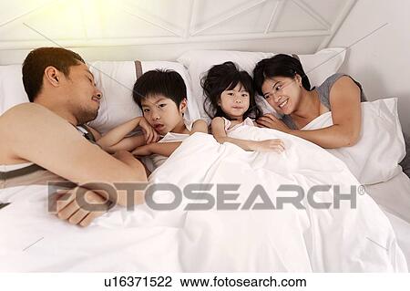 Young Chinese family of parents and two young children laying in bed together at home View Large Photo Image Stock Image - Young Chinese family of parents and two young children laying in bed together at home. Fotosearch