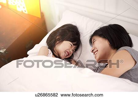 Young Chinese mother and daughter laying in bed together at home View Large Photo Image Stock Image - Young Chinese mother and daughter laying in bed together at home. Fotosearch
