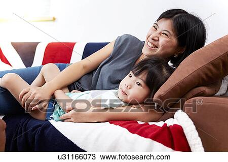 Young Chinese mother and daughter laying on sofa watching the television together at home View Large Photo Image Stock Image - Young Chinese mother and daughter laying on sofa watching the television together at home. Fotosearch
