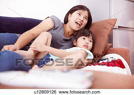 Young Chinese mother and daughter laying on sofa watching the television together at home View Large Photo Image Stock Photograph - Young Chinese mother and daughter laying on sofa watching the television together at home. Fotosearch
