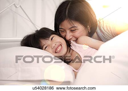 Stock Photograph - Young Chinese mother and daughter laying in bed together at home. Fotosearch