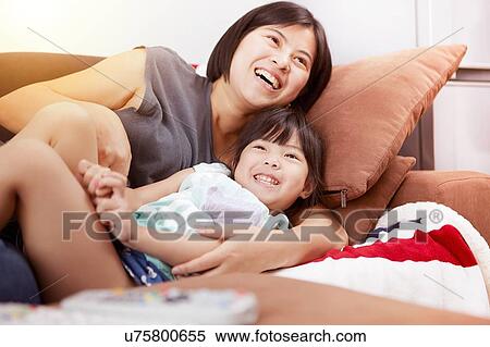 Young Chinese mother and daughter laying on sofa watching the television together at home View Large Photo Image Stock Photography - Young Chinese mother and daughter laying on sofa watching the television together at home. Fotosearch