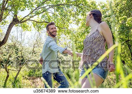 Young couple holding hands in forest fooling around smiling View Large Photo Image Stock Photo - Young couple holding hands in forest fooling around smiling. Fotosearch