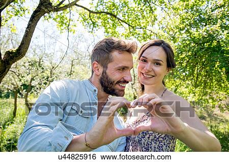 Young couple making heart shape with hands, looking at camera smiling View Large Photo Image Stock Photograph - Young couple making heart shape with hands, looking at camera smiling. Fotosearch