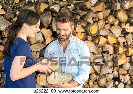 Stock Image - Young couple selecting chopped firewood from pile. Fotosearch