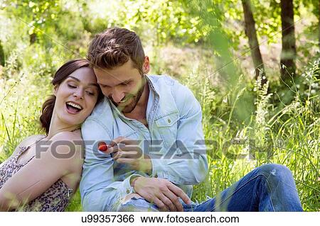 Young couple sitting back to back on grass holding strawberry smiling View Large Photo Image Stock Photograph - Young couple sitting back to back on grass holding strawberry smiling. Fotosearch