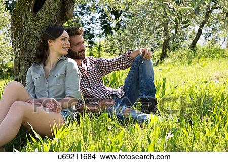 Picture - Young couple sitting leaning against tree together. Fotosearch