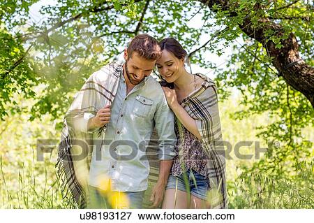 Stock Photo - Young couple walking wrapped in blanket looking down smiling. Fotosearch