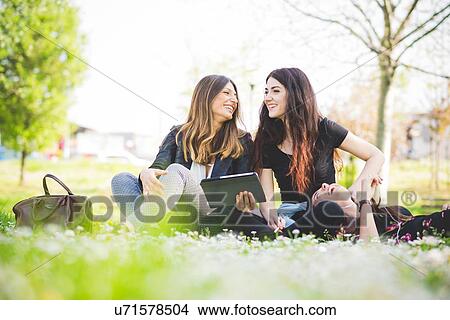 Picture - Young female friends relaxing and chatting in park. Fotosearch