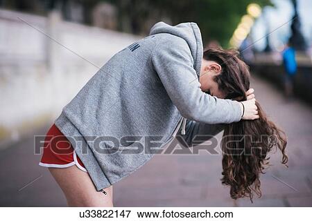 Stock Photo - Young female runner tying up long hair on riverside. Fotosearch
