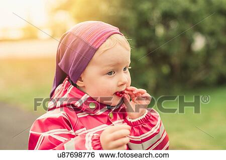 Stock Photograph - Young girl eating redcurrants, outdoors. Fotosearch
