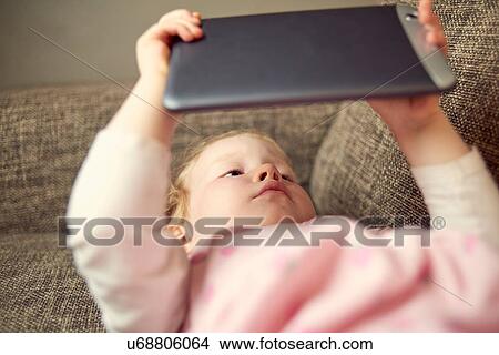 Young girl lying on sofa, holding digital tablet View Large Photo Image Picture - Young girl lying on sofa, holding digital tablet. Fotosearch