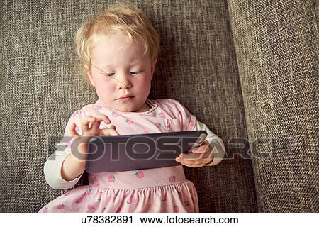Young girl lying on sofa, holding digital tablet View Large Photo Image Stock Image - Young girl lying on sofa, holding digital tablet. Fotosearch