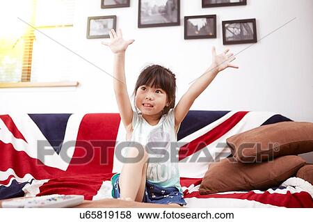 Stock Photo - Young girl sitting on sofa watching the television at home. Fotosearch