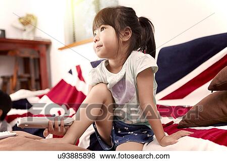 Stock Photo - Young girl sitting on sofa watching the television at home. Fotosearch