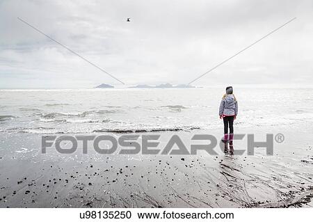 Young girl, standing on beach, looking at view, rear view, Landeyjahofn, Iceland View Large Photo Image Stock Image - Young girl, standing on beach, looking at view, rear view, Landeyjahofn, Iceland. Fotosearch