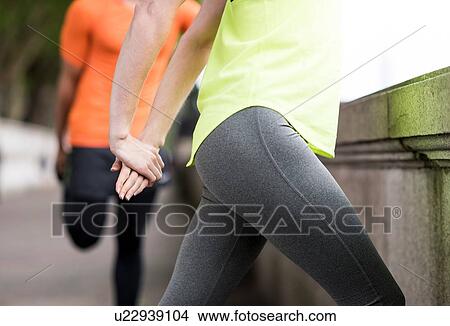 Picture - Young male and female city runners stretching legs. Fotosearch