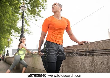 Stock Image - Young male and female city runners warming up. Fotosearch
