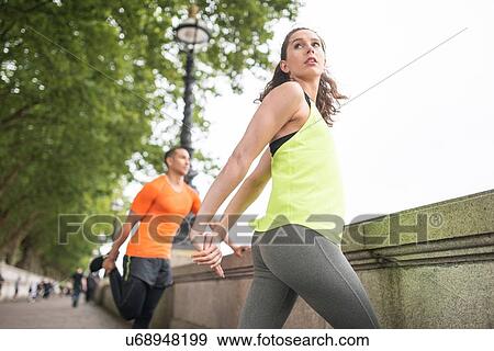 Stock Photo - Young male and female runners warming up on riverside. Fotosearch