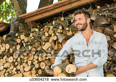 Stock Photo - Young man holding chopped firewood looking away smiling. Fotosearch