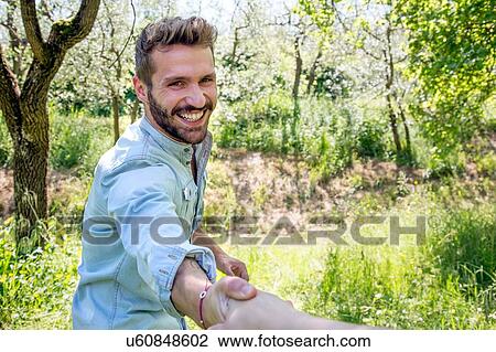 Stock Image - Young man holding hand looking at camera smiling. Fotosearch