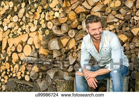 Picture - Young man sitting in front of chopped wood. Fotosearch