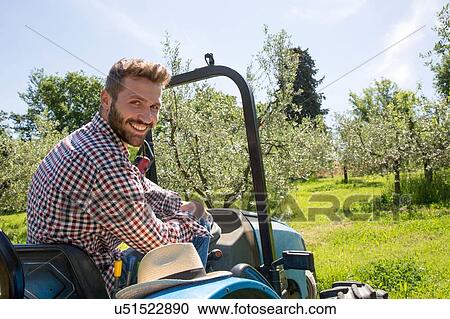 Young man sitting in tractor looking over shoulder at camera smiling View Large Photo Image Stock Image - Young man sitting in tractor looking over shoulder at camera smiling. Fotosearch