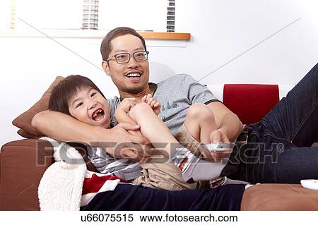 Stock Photography - Young, modern Chinese family of father and young son sitting on sofa watching television together at home. Fotosearch
