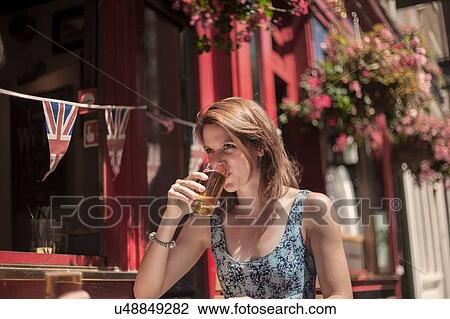 Stock Image - Young woman drinking beer sitting outside traditional pub. Fotosearch