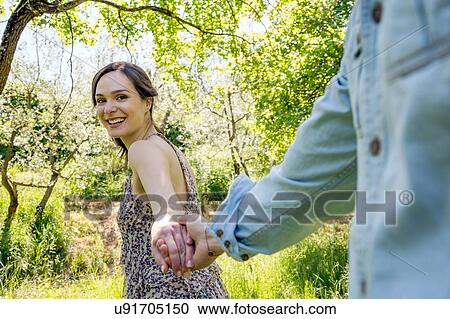Stock Image - Young woman leading young man through forest, holding hand. Fotosearch