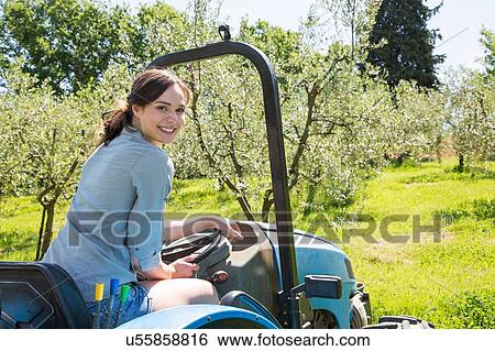 Young woman sitting in tractor looking over shoulder at camera smiling View Large Photo Image Stock Photograph - Young woman sitting in tractor looking over shoulder at camera smiling. Fotosearch
