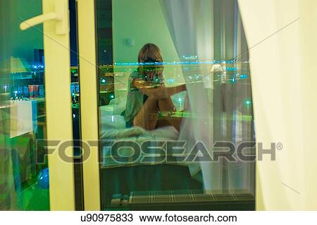 Young woman sitting on bed in room View Large Photo Image Stock Image - Young woman sitting on bed in room. Fotosearch