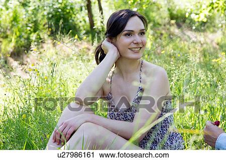 Young woman sitting on grass looking away smiling View Large Photo Image Stock Image - Young woman sitting on grass looking away smiling. Fotosearch