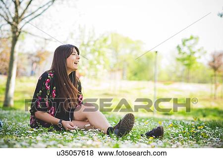 Young woman sitting on park grass listening to earphones View Large Photo Image Stock Photo - Young woman sitting on park grass listening to earphones. Fotosearch