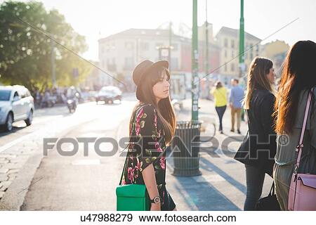 Stock Photo - Young woman strolling behind friends in city. Fotosearch