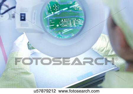 Stock Image - Young woman using magnifier at quality check station at factory producing flexible electronic circuit boards. Plant is located in the south of China, in Zhuhai, Guangdong province. Fotosearch