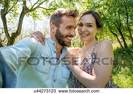 Stock Image - Young woman with arm around young man looking at camera smiling. Fotosearch