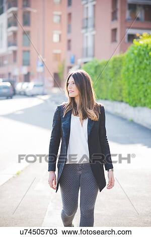 Stock Image - Young woman with long brown hair strolling and looking sideward. Fotosearch