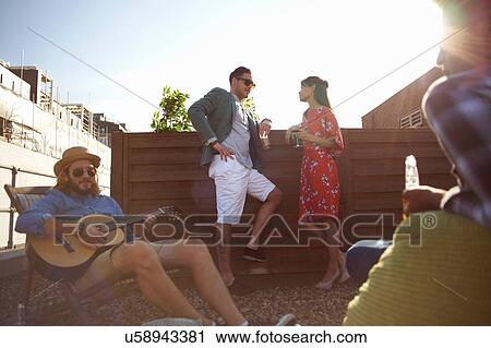 Adult friends chatting and playing guitar at rooftop party View Large Photo Image Stock Image - Adult friends chatting and playing guitar at rooftop party. Fotosearch