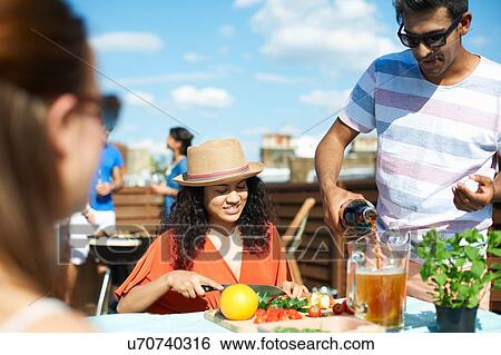 Stock Photograph - Adult friends preparing fresh punch cocktail at rooftop party. Fotosearch