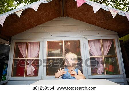 Picture - Baby girl sitting at table in front of playhouse looking away. Fotosearch
