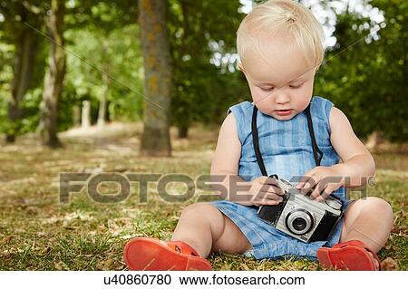 Baby girl sitting on grass holding film camera looking down View Large Photo Image Stock Image - Baby girl sitting on grass holding film camera looking down. Fotosearch