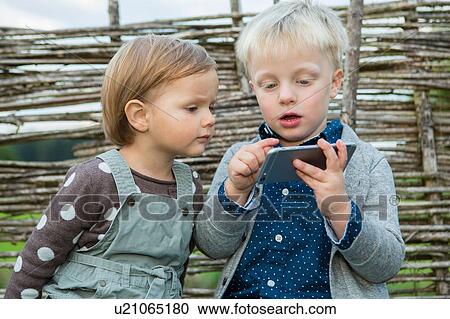 Boy and female toddler using touchscreen on smartphone in garden View Large Photo Image Stock Image - Boy and female toddler using touchscreen on smartphone in garden. Fotosearch